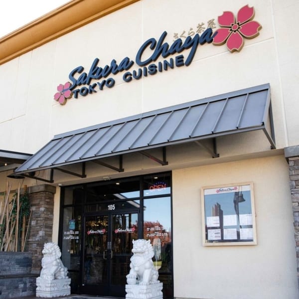 Exterior of Sakura Chaya Japanese restaurant with a black awning, glass doors, and two foo dog statues.