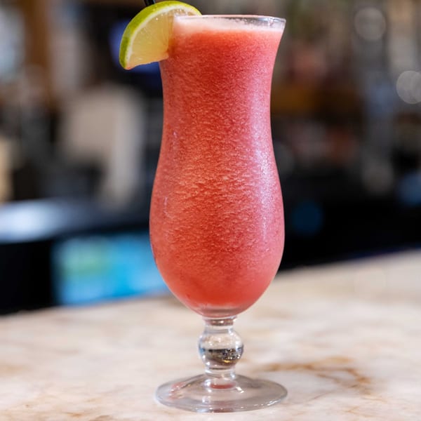 A vibrant red frozen cocktail with a lime wedge and straw, on a marble bar.