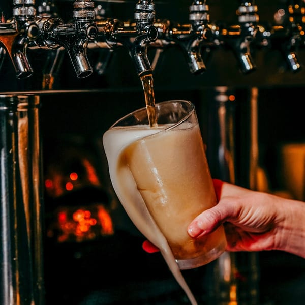 A hand holding a glass being filled with beer from a tap, overflowing with foam.