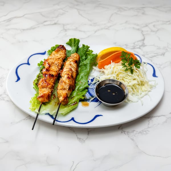 Two chicken skewers with sesame seeds on lettuce, with shredded cabbage, orange slices, and soy sauce.
