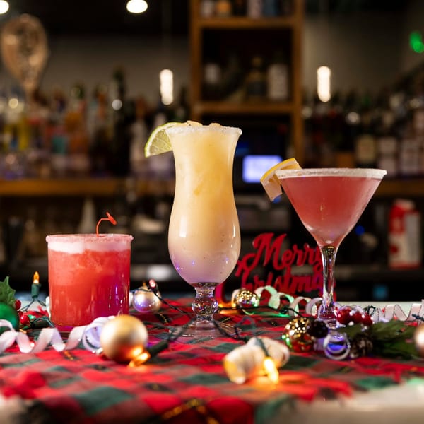Three festive cocktails, two red and one yellow, on a plaid tablecloth with Christmas decorations.