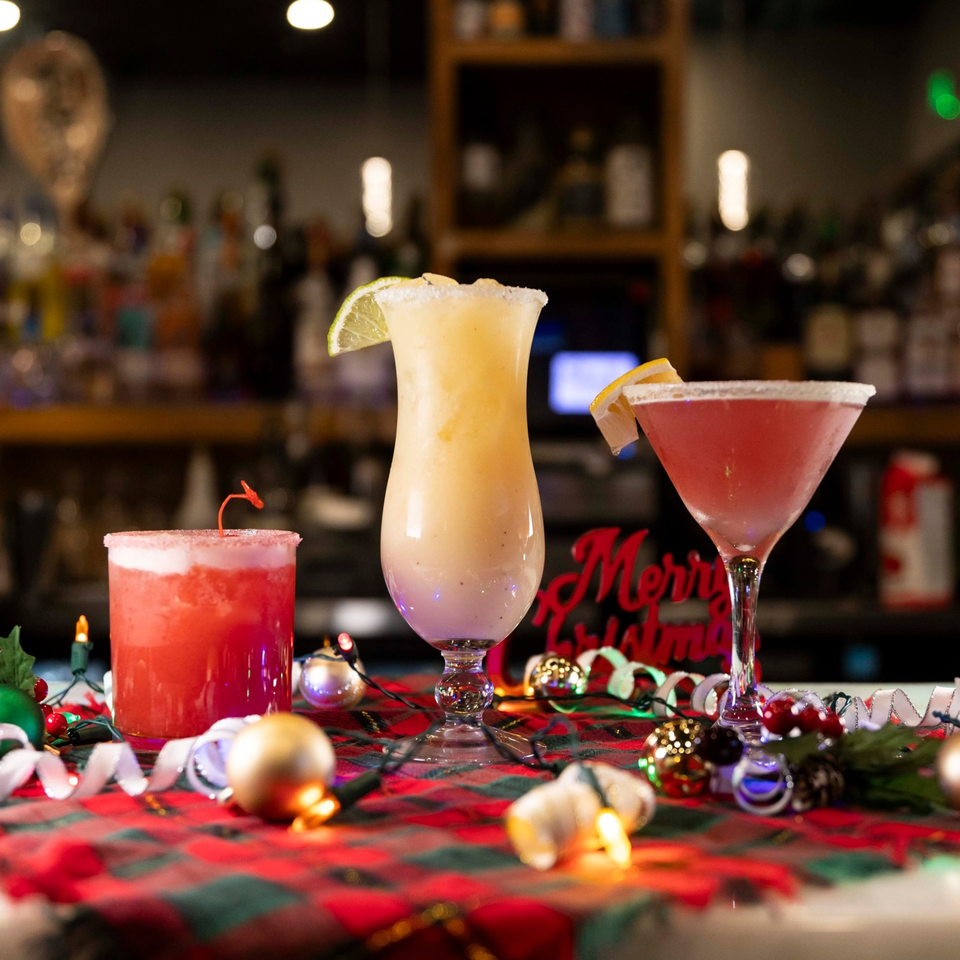 Three festive cocktails, two red and one yellow, on a plaid tablecloth with Christmas decorations.