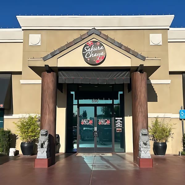 Exterior of Sakura Chaya Japanese restaurant with a prominent sign, glass doors, and two stone lion statues.