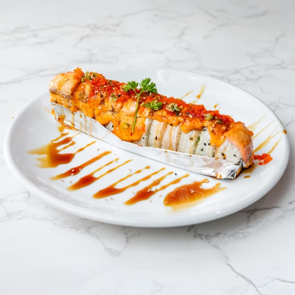 Sakura Chaya's baked salmon roll, topped with spicy sauce, tobiko, and green onions, on a white plate.