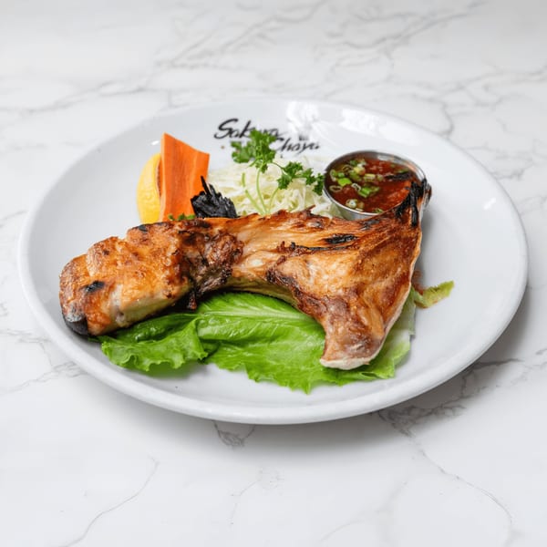Grilled fish collar with lemon, shredded cabbage, and dipping sauce on a white plate.