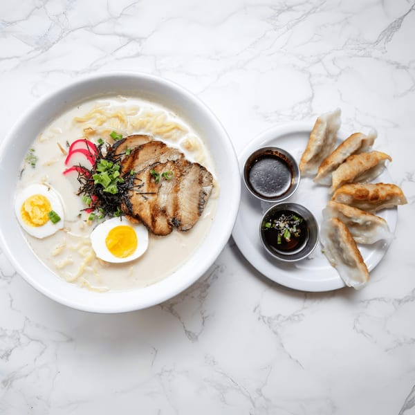 A bowl of Sakura Chaya ramen with pork, egg, and fish cake, alongside a plate of gyoza.