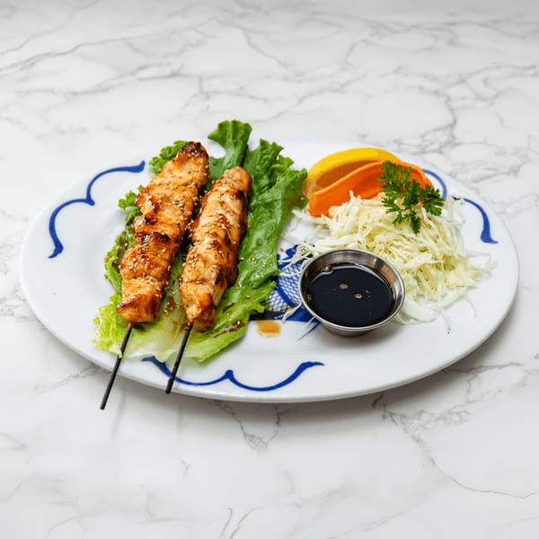 Two chicken skewers with sesame seeds on lettuce, with shredded cabbage, orange slices, and soy sauce.